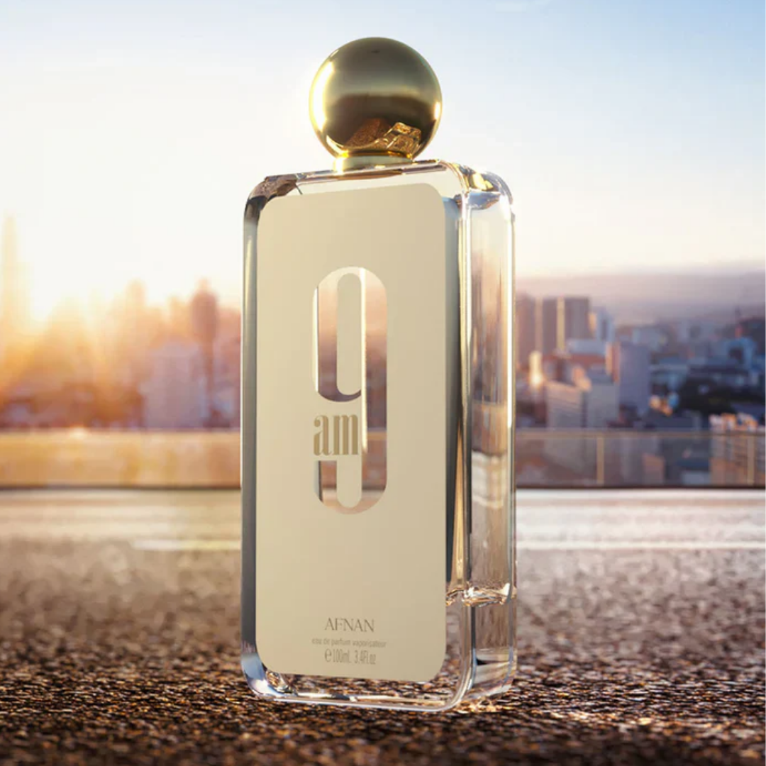 Perfume bottle with gold cap on a textured surface with a cityscape in the background. Afnan 9am Womens Perfume