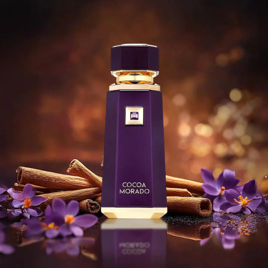 Purple perfume bottle labeled 'Cocoa Morado' with cinnamon sticks and purple flowers on a reflective surface.