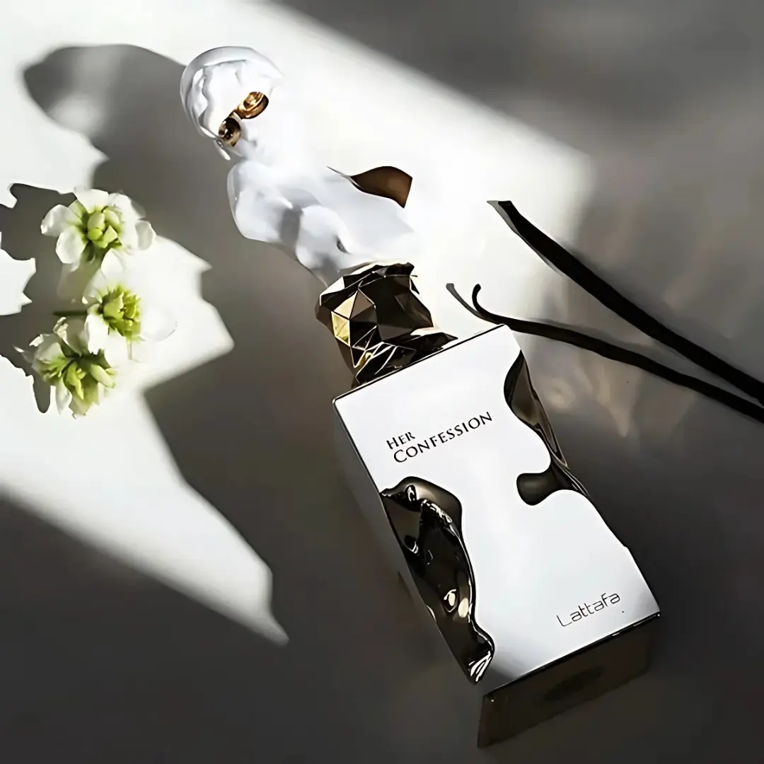 Perfume bottle labeled 'Her Confession' by Lattafa Perfumes on a reflective surface with flowers.