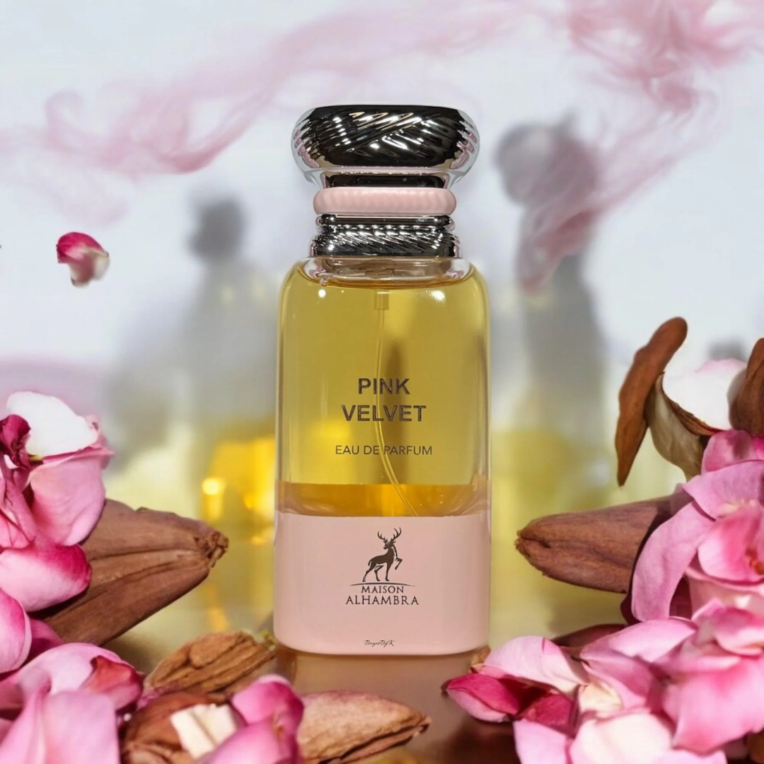Perfume bottle labeled 'Pink Velvet' surrounded by pink flowers and leaves on a soft, blurred background.
