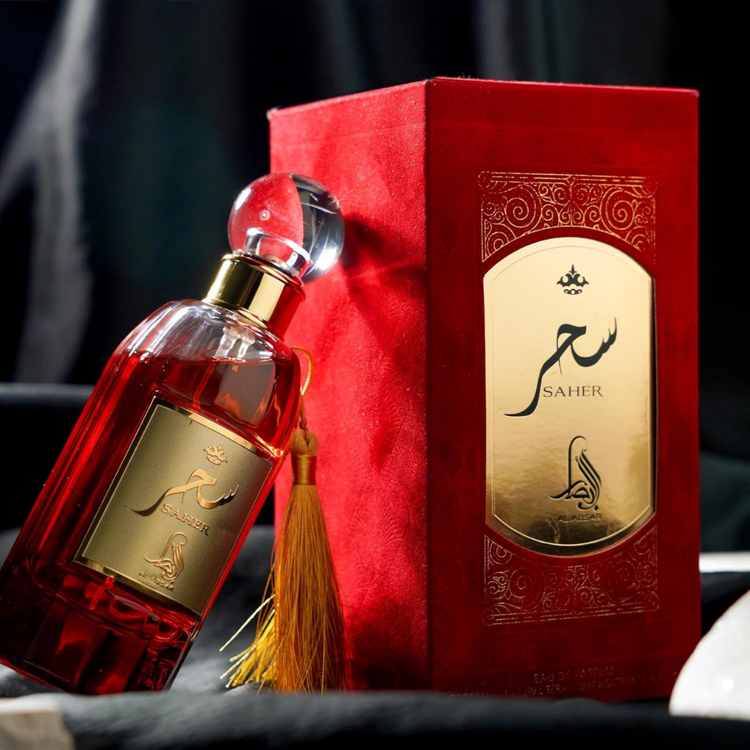 Red perfume bottle with gold label and tassel next to a matching red box on a dark background. Saher by Al Absar Womens Perfume