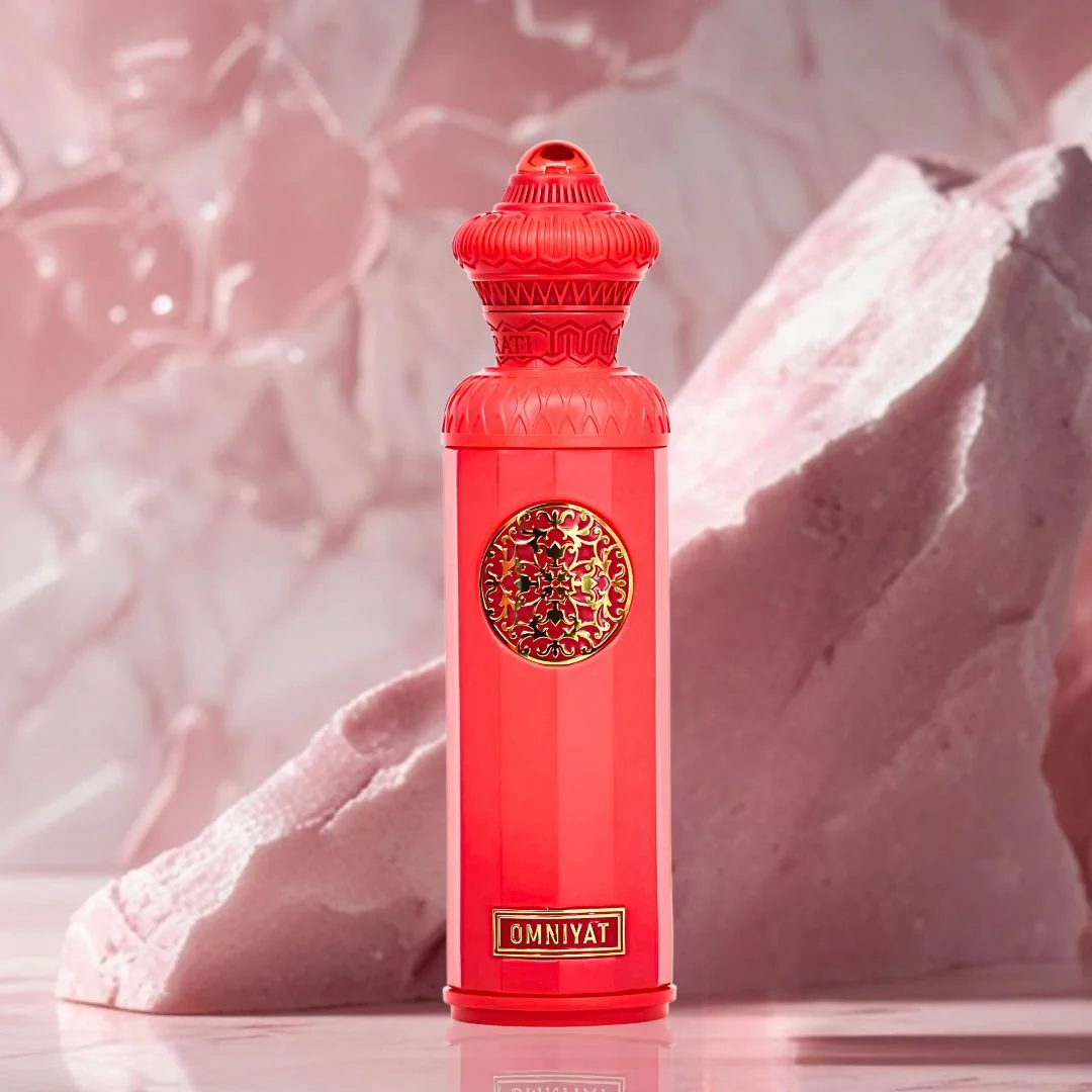 Red bottle with intricate design and 'Omnivat' branding on a textured pink background. Surrati Omniyat Unisex Perfume