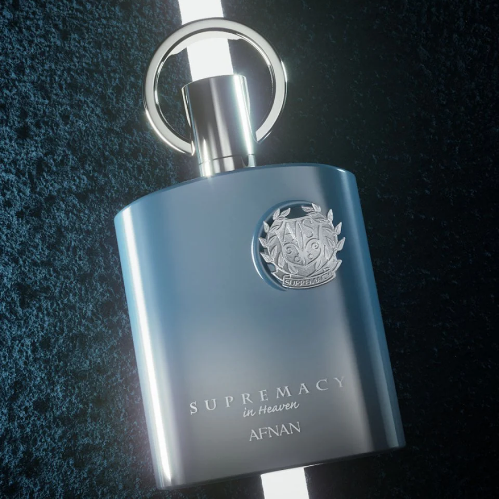 A metallic blue bottle of Afnan 'Supremacy in Heaven' perfume with a silver emblem and keychain ring, set against a dark textured background.