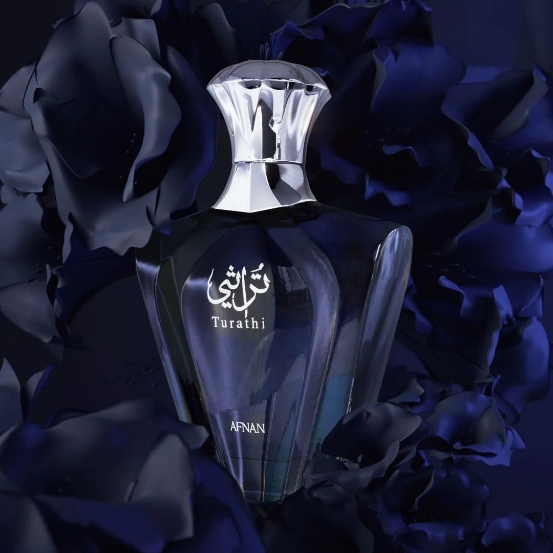 A dark glass perfume bottle with a reflective silver cap, labeled 'Turathi' and 'AFNAN', centered against a background of dark blue and black rose petals.