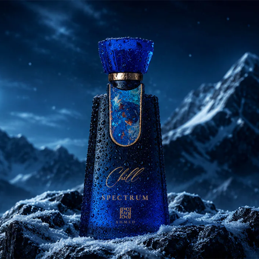 A dark blue glass perfume bottle labeled 'Chill SPECTRUM' with gold lettering, standing on snowy rocks against a dramatic mountain night sky. The bottle is covered in water droplets, and the background shows snow-covered peaks under a starry sky.