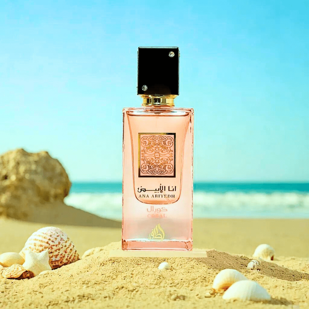 Ana Abiyedh Coral by Lattafa – pink perfume bottle photographed on sandy beach with seashells, evoking tropical and summer vibes. 