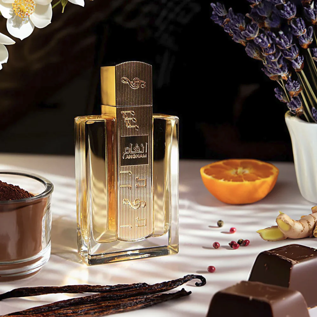 Gold perfume bottle on a table with vanilla beans, chocolate, and an orange. Angham by Lattafa 100ml perfume