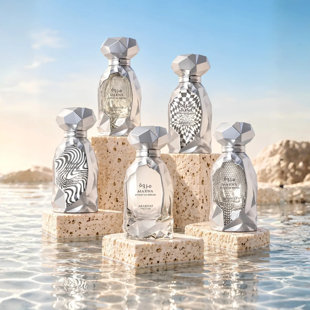 Five faceted silver perfume bottles with unique printed patterns, displayed on beige stone pedestals in shallow water under a blue sky. Arabiyat Prestige: Marwa Extrait