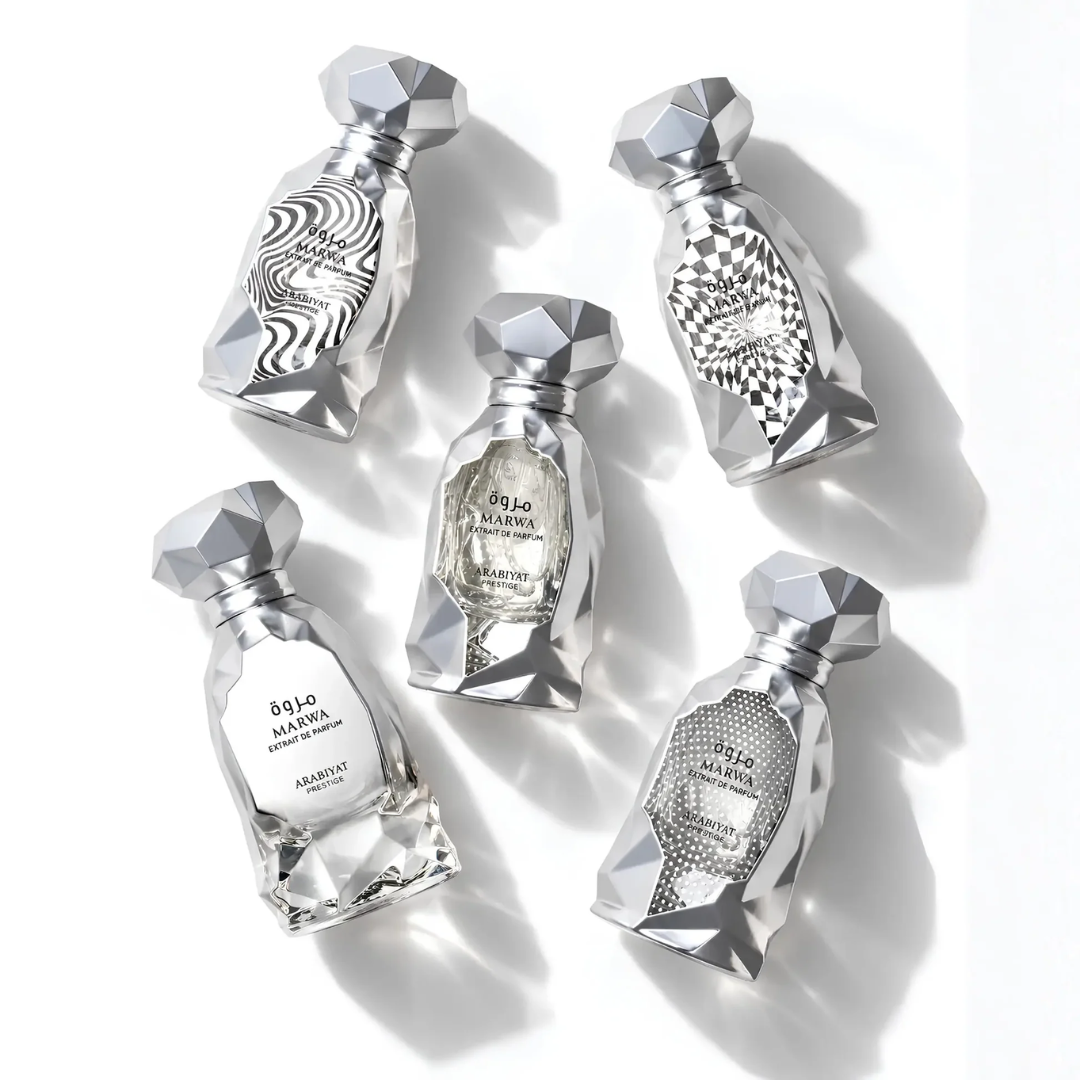 Five faceted silver perfume bottles arranged on a white background, each with a different abstract printed label design. The bottles are made of a reflective metallic material with geometric crystal-like tops and bases. Arabiyat Prestige: Marwa Extrait