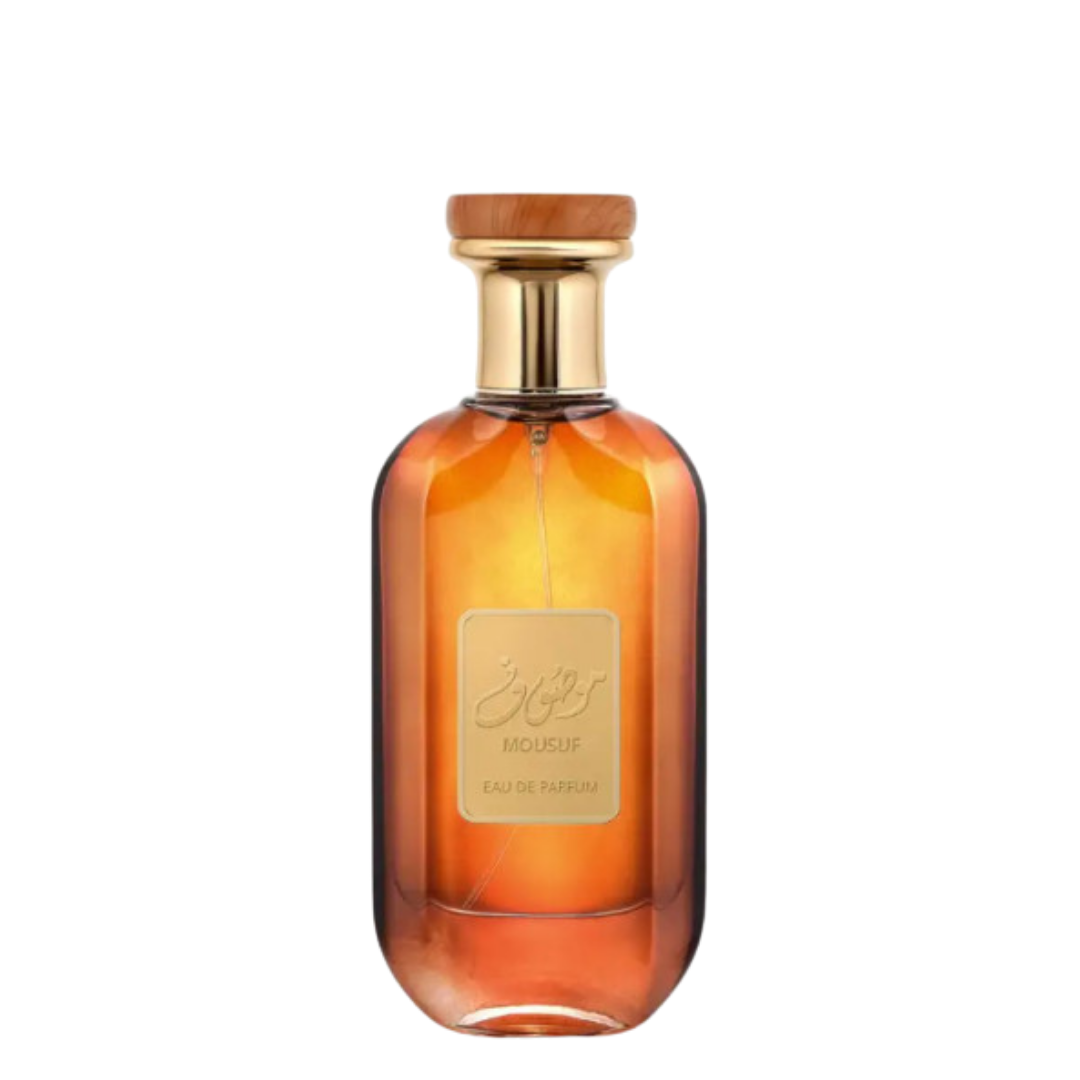 A glass bottle of Mousuf Perfume by Ard Al Zaafaran with a wooden cap and a label in front, displaying the name and fragrance type.  Amber Gradient Mousuf Perfume Bottle – Elegant amber gradient glass bottle of Mousuf Eau de Parfum with a gold and wood-accented cap, exuding luxury and oriental fragrance allure.