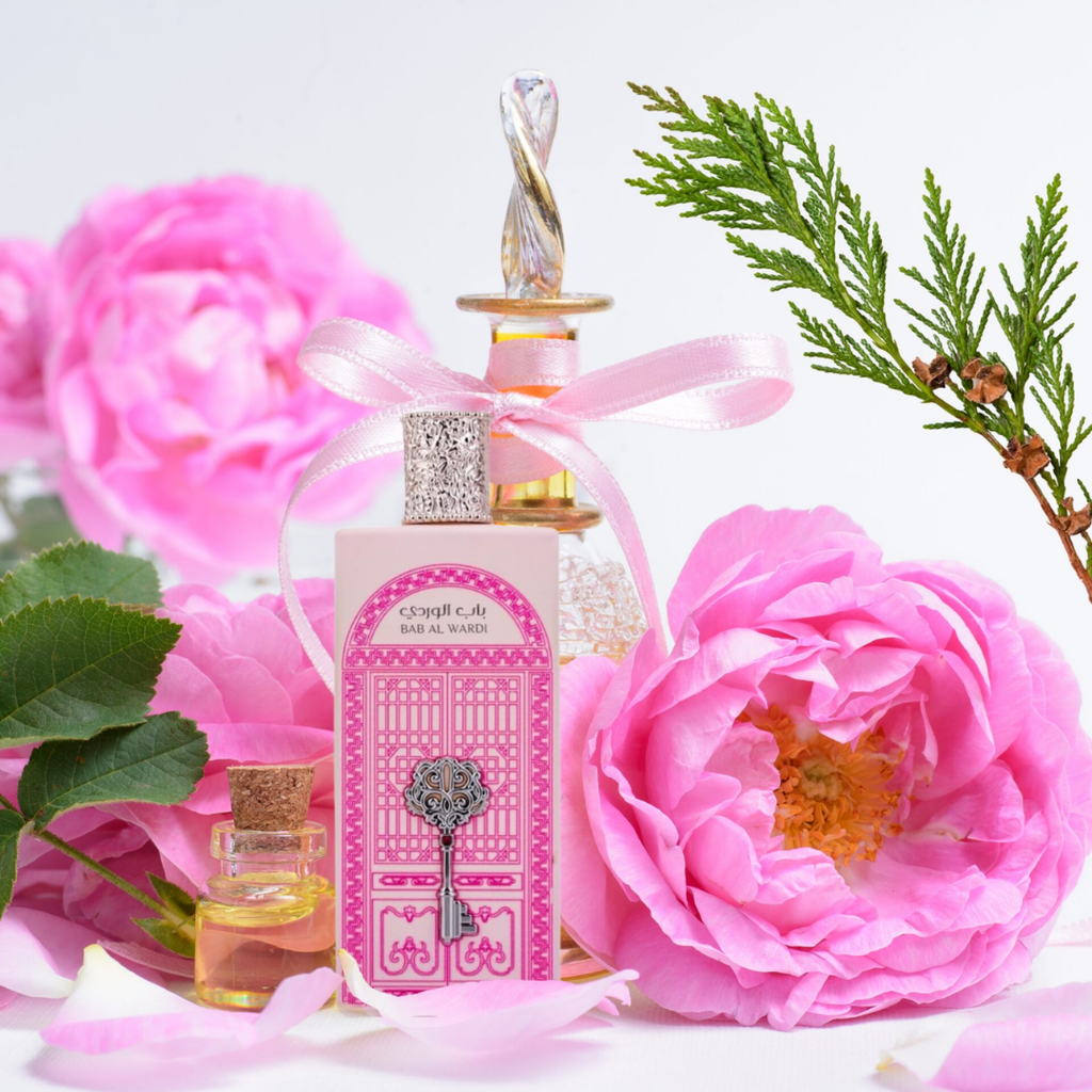Perfume bottle with decorative cap surrounded by pink flowers and green leaves. Bab Al Wardi by Ard Al Zaafaran Womens Perfume