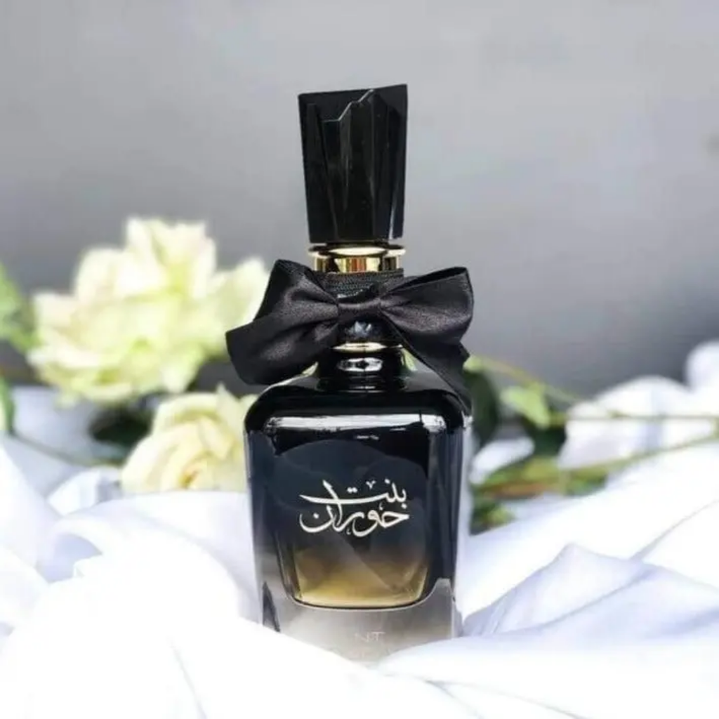 Perfume bottle with black cap and ribbon on white fabric with flowers in background. Bint Hooran Womens Perfume by Ard Al Zaafaran