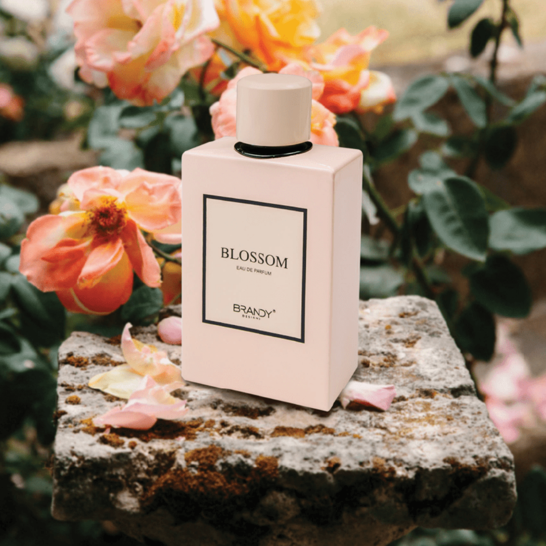 Perfume bottle labeled 'Blossom' by Brandy on a stone surface with flowers in the background. Blossom by Brandy Designs Womens Perfume