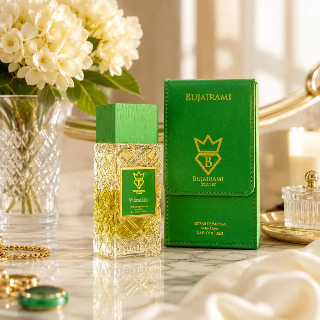 Bujairami Vibration perfume bottle and its green box on a marble surface, styled with white flowers, gold jewelry, and soft warm lighting.