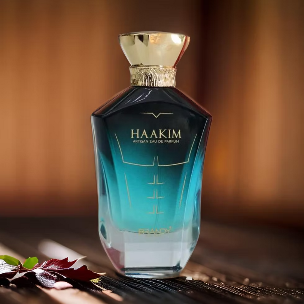Haakim perfume bottle with a gold cap on a wooden surface with leaves. Haakim by Brandy Designs Mens Perfume