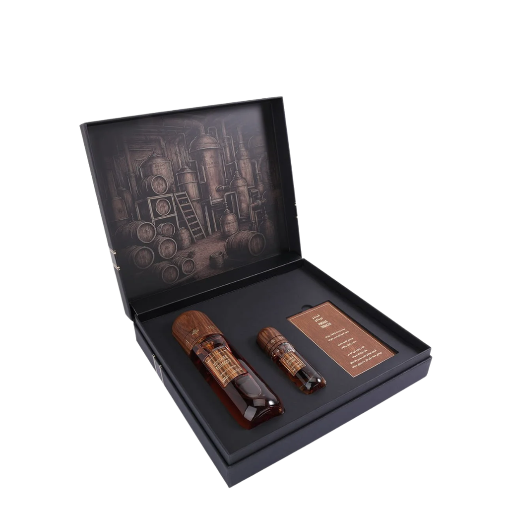 A premium gift set in an open black presentation box, containing two amber glass bottles with gold labels and a small brown card, set against a plain white background. IBRAQ: Vintage Tobacco Collection
