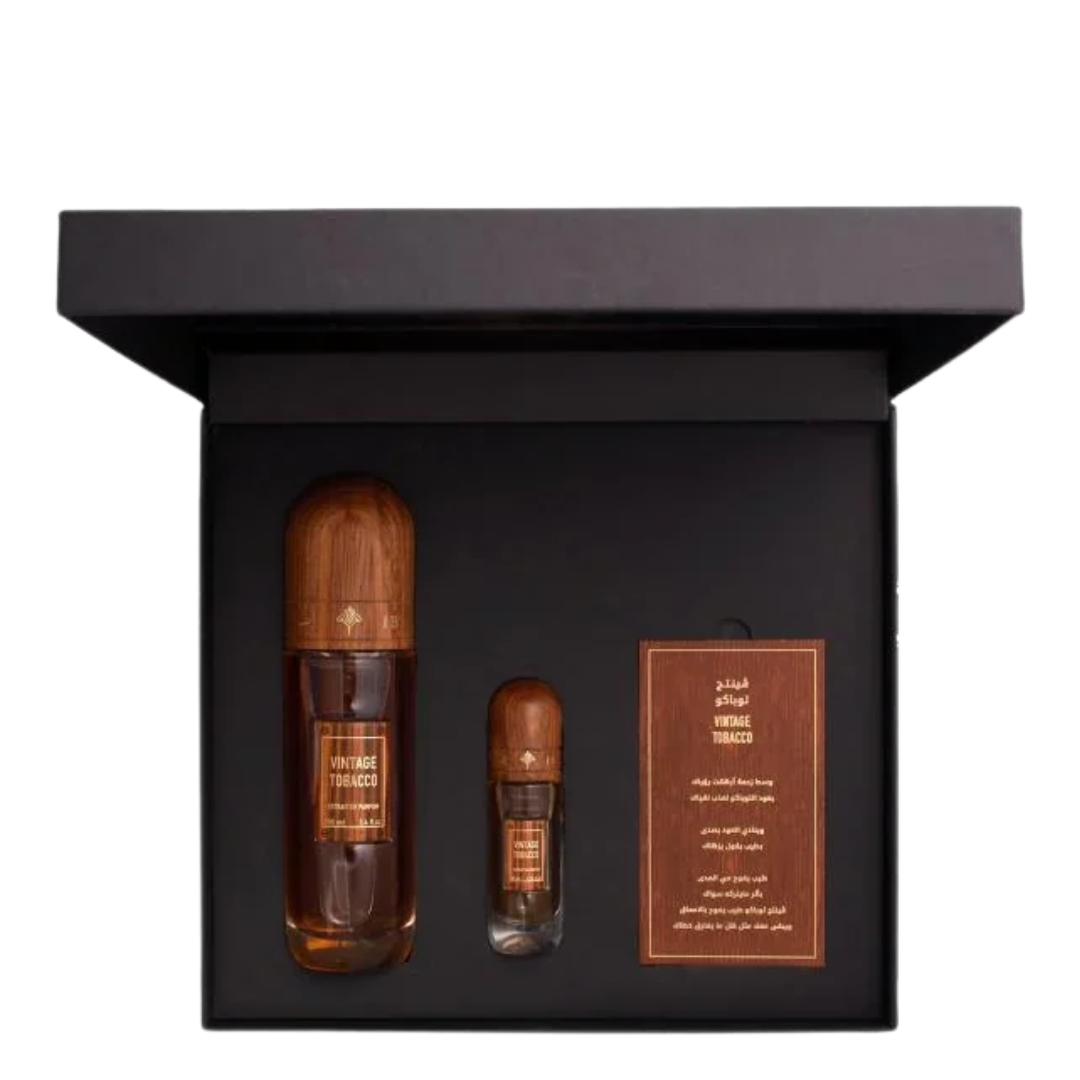 A luxury fragrance gift set in a black presentation box, featuring a large amber glass bottle, a smaller sample vial, and a brown leather card with Arabic text. IBRAQ: Vintage Tobacco Collection