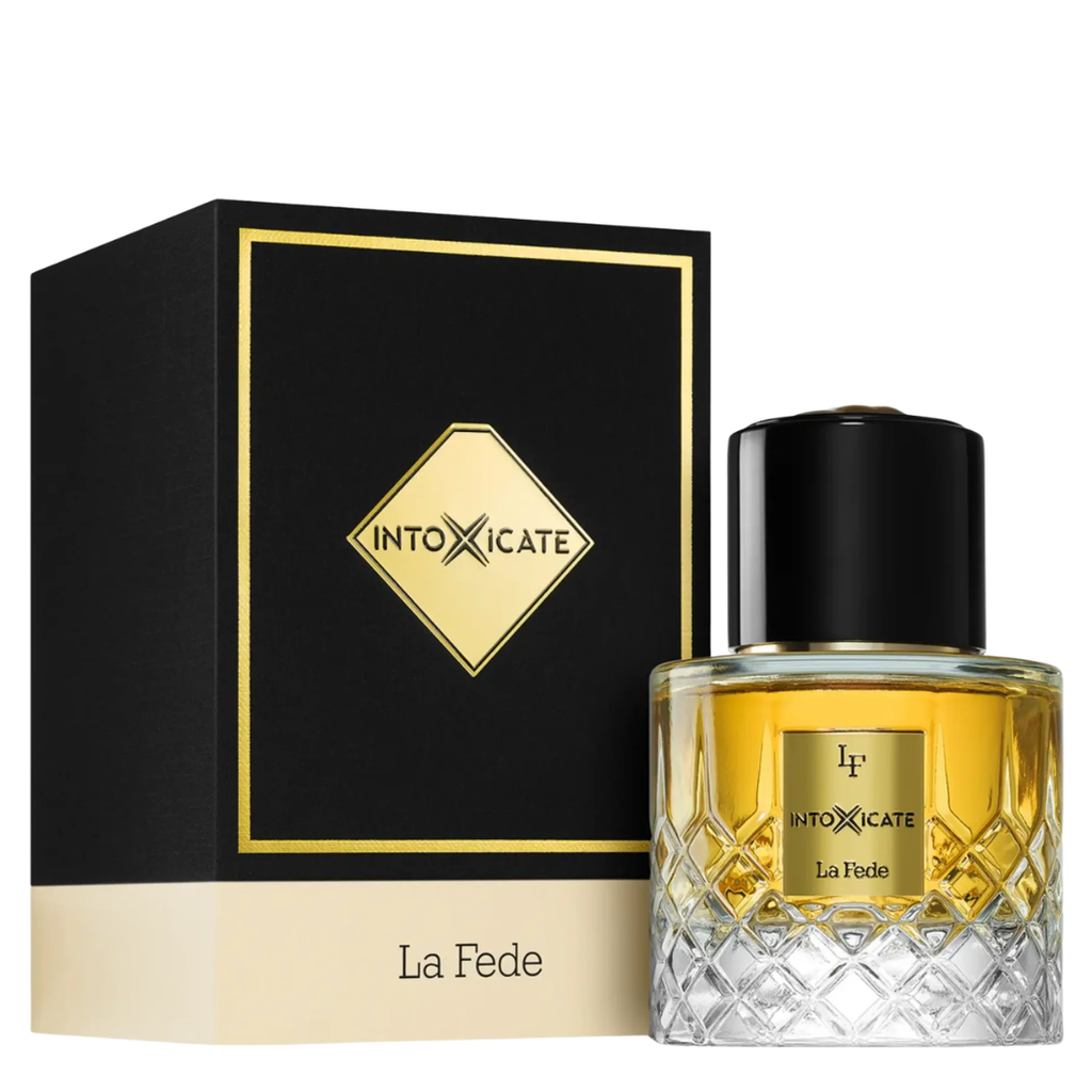 A bottle of INTOXICATE La Fede perfume with a black cap and a faceted clear glass body showing golden-yellow liquid, displayed next to its black and gold box on a white background.