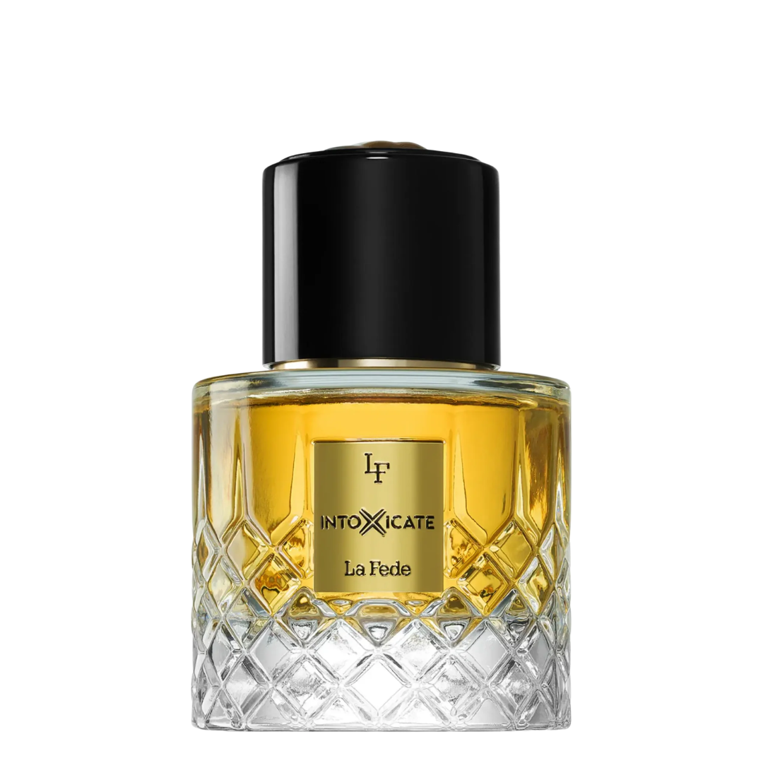 A bottle of La Fede Intoxicate perfume by Khadlaj, featuring a clear glass bottle with a diamond-cut pattern, filled with golden-yellow liquid, a gold label, and a glossy black cap, set against a plain white background.