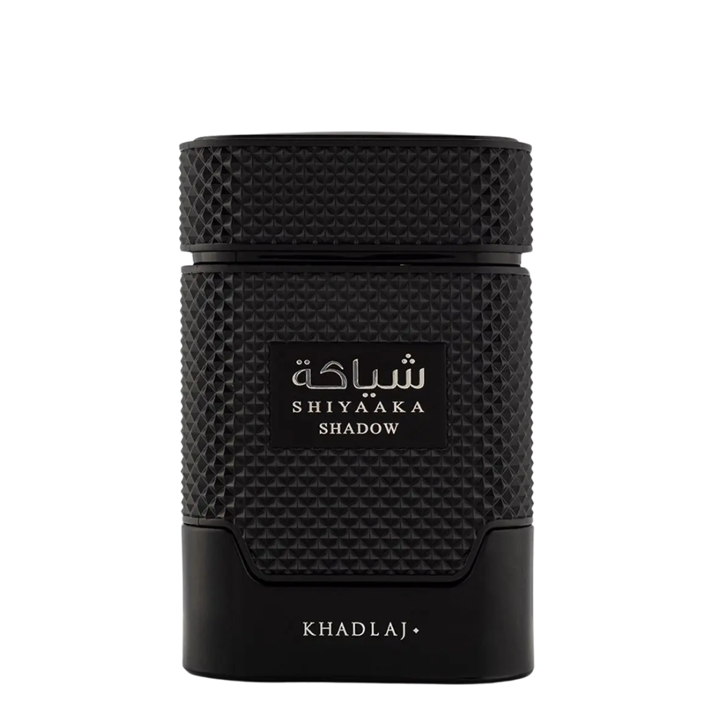 A black textured cylindrical perfume bottle with a textured cap, featuring a black label with white Arabic script and 'SHIYAAKA SHADOW' in English, and 'KHADLAJ+' printed at the bottom, set against a plain white background.