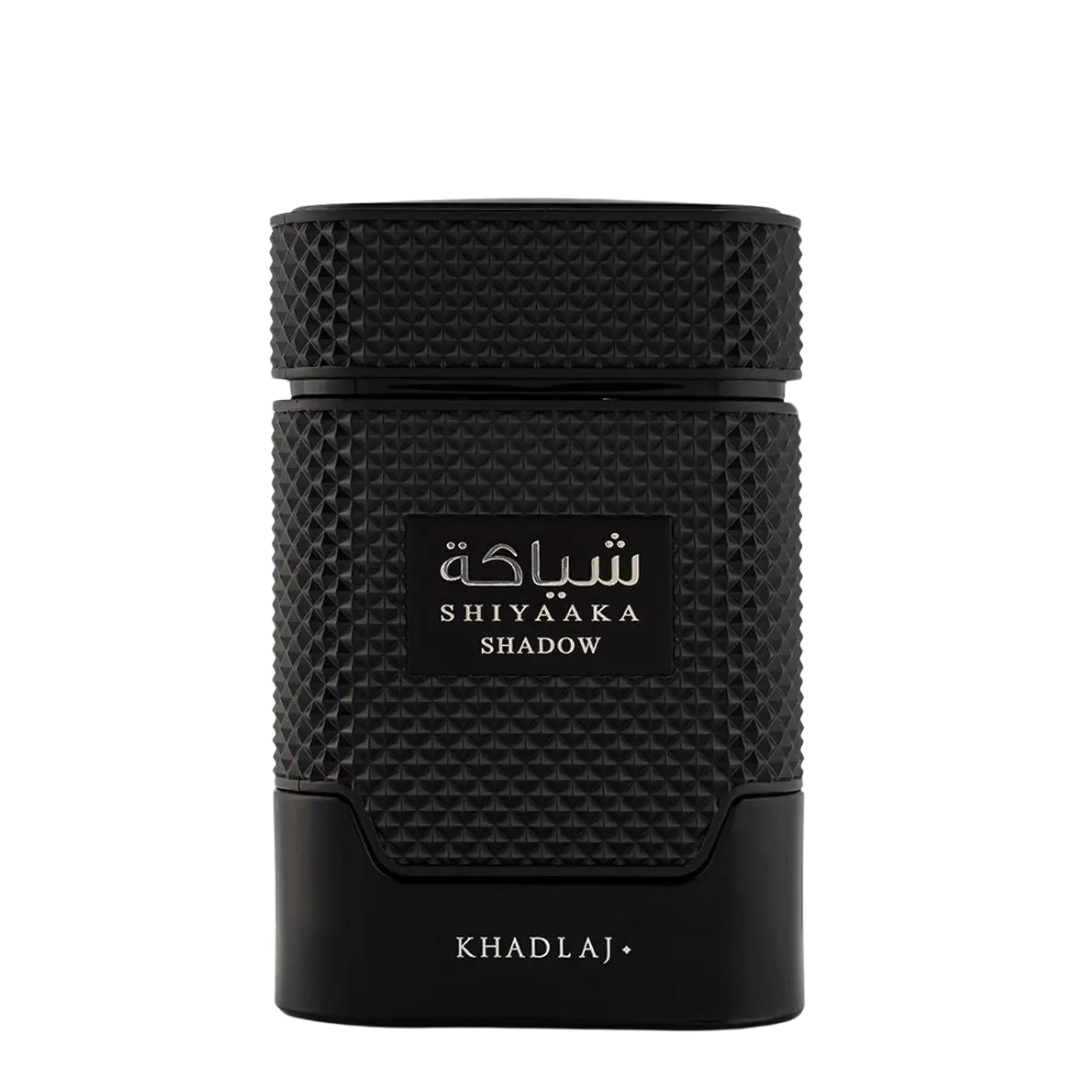 A black textured cylindrical perfume bottle with a textured cap, featuring a black label with white Arabic script and 'SHIYAAKA SHADOW' in English, and 'KHADLAJ+' printed at the bottom, set against a plain white background.