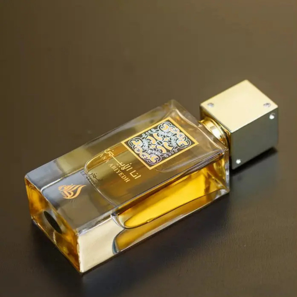 Lattafa Ana Abiyedh Leather bottle lying flat – Golden-capped rectangular glass fragrance bottle resting on a dark surface, showcasing rich amber perfume liquid and ornate black-and-gold label. 
