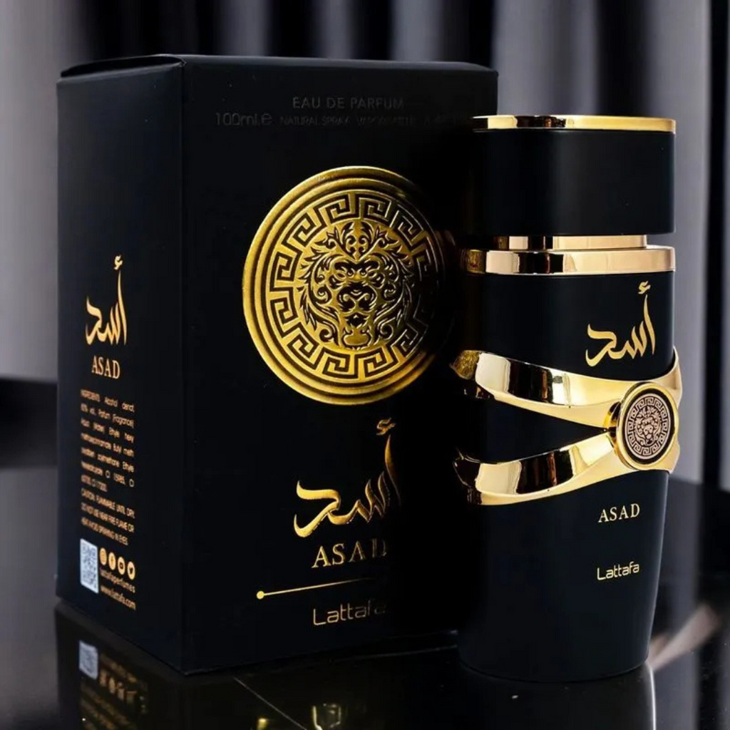 Asad by Lattafa perfume with luxury box – Matte black fragrance bottle with golden details beside matching gold-accented packaging on a reflective black surface. 