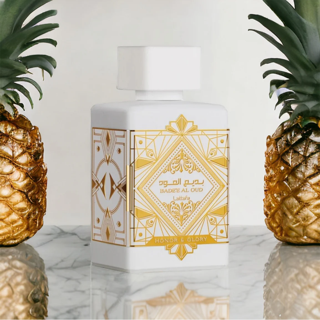 Perfume bottle with gold and white design between two gold pineapples. Lattafa Badee Al Oud Honor & Glory Unisex Perfume
