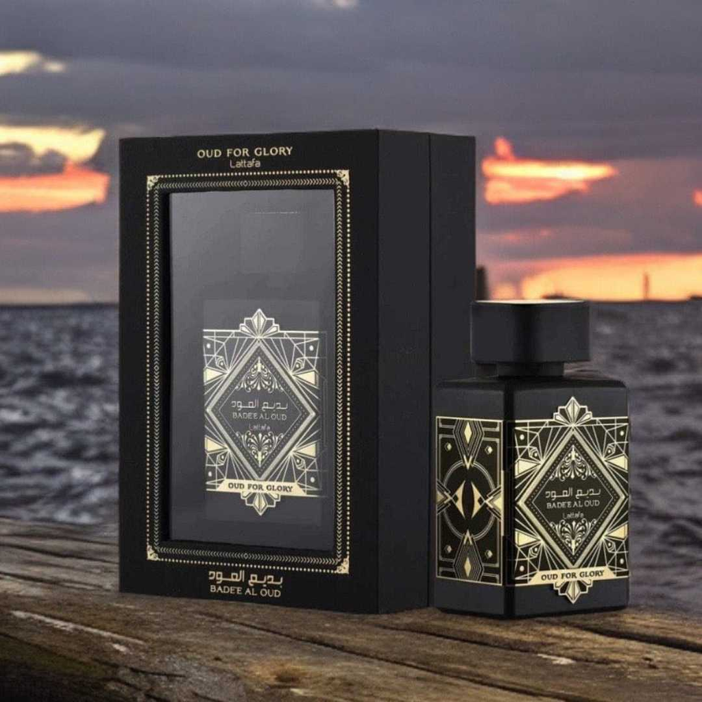Perfume bottle and packaging on wooden surface with sunset over sea. Lattafa Badee Al Oud Unisex Perfume