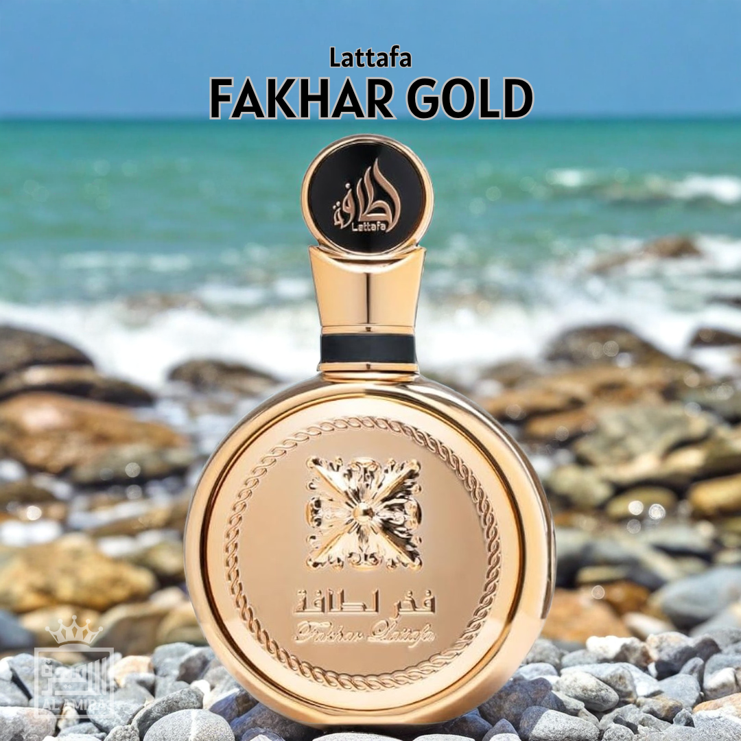 Gold Lattafa Fakhar Gold perfume bottle on a rocky beach with ocean in the background. 