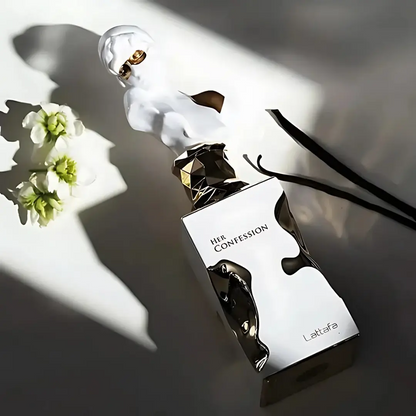 Perfume bottle labeled 'Her Confession' by Lattafa Perfumes on a reflective surface with flowers.