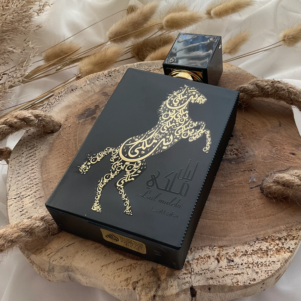 Black box with gold intricate design on a wooden surface with dried plants. Lattafa Lail Maleki Unisex Perfume