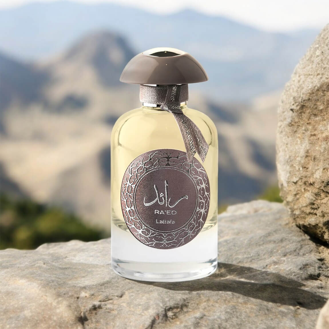 Perfume bottle with decorative label on a rock with mountain background. Lattafa Ra'ed Silver Unisex Perfume