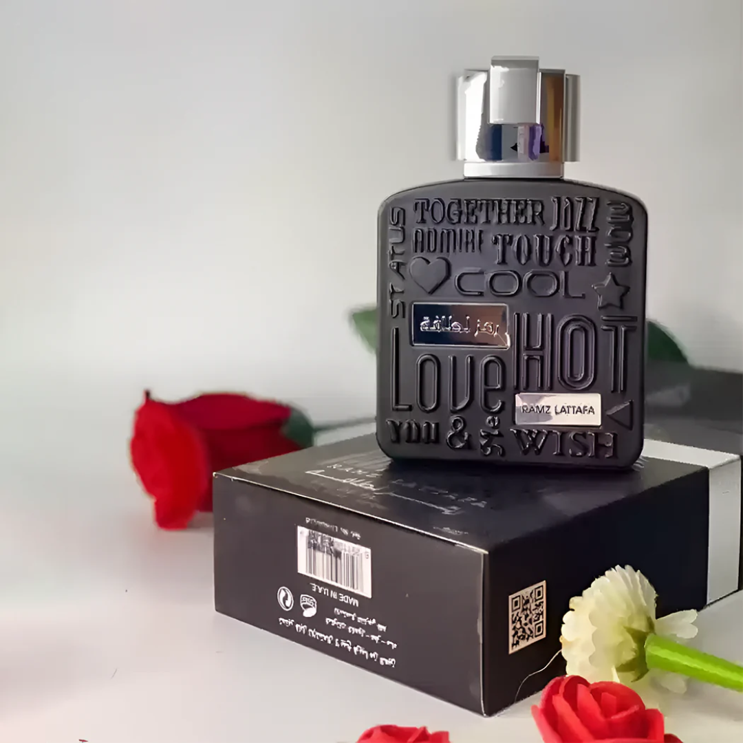 Perfume bottle with decorative text on a box, surrounded by flowers. Lattafa Ramz Silver Unisex Perfume