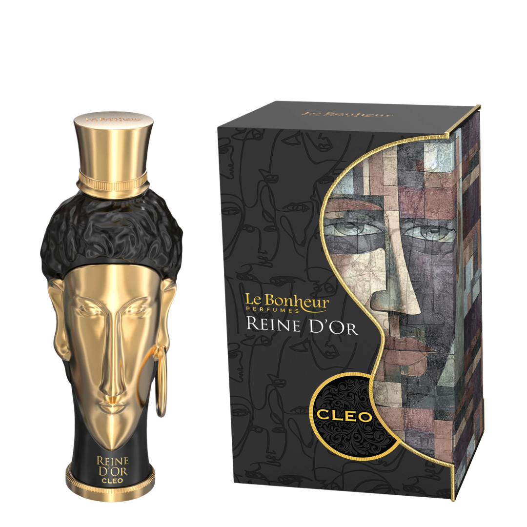 A bottle of Cleo Reine D'Or perfume next to its retail box. The bottle is shaped like a gold and black sculpted head with a gold cap, and the box features a black background with a stylized face illustration and gold lettering. Le Bonheur: Reine d'Or Cleo