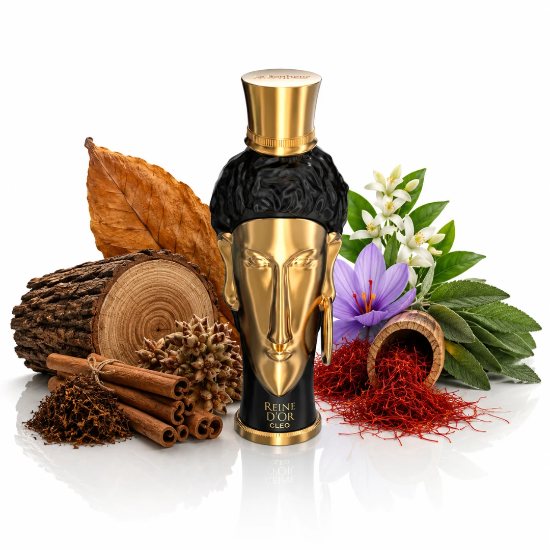A perfume bottle labeled 'REINE D'OR CLEO' stands centered on a white reflective surface, surrounded by natural ingredients including a cinnamon stick bundle, dried leaves, a log slice, saffron threads, purple flowers, and green leaves. Le Bonheur: Reine d'Or Cleo