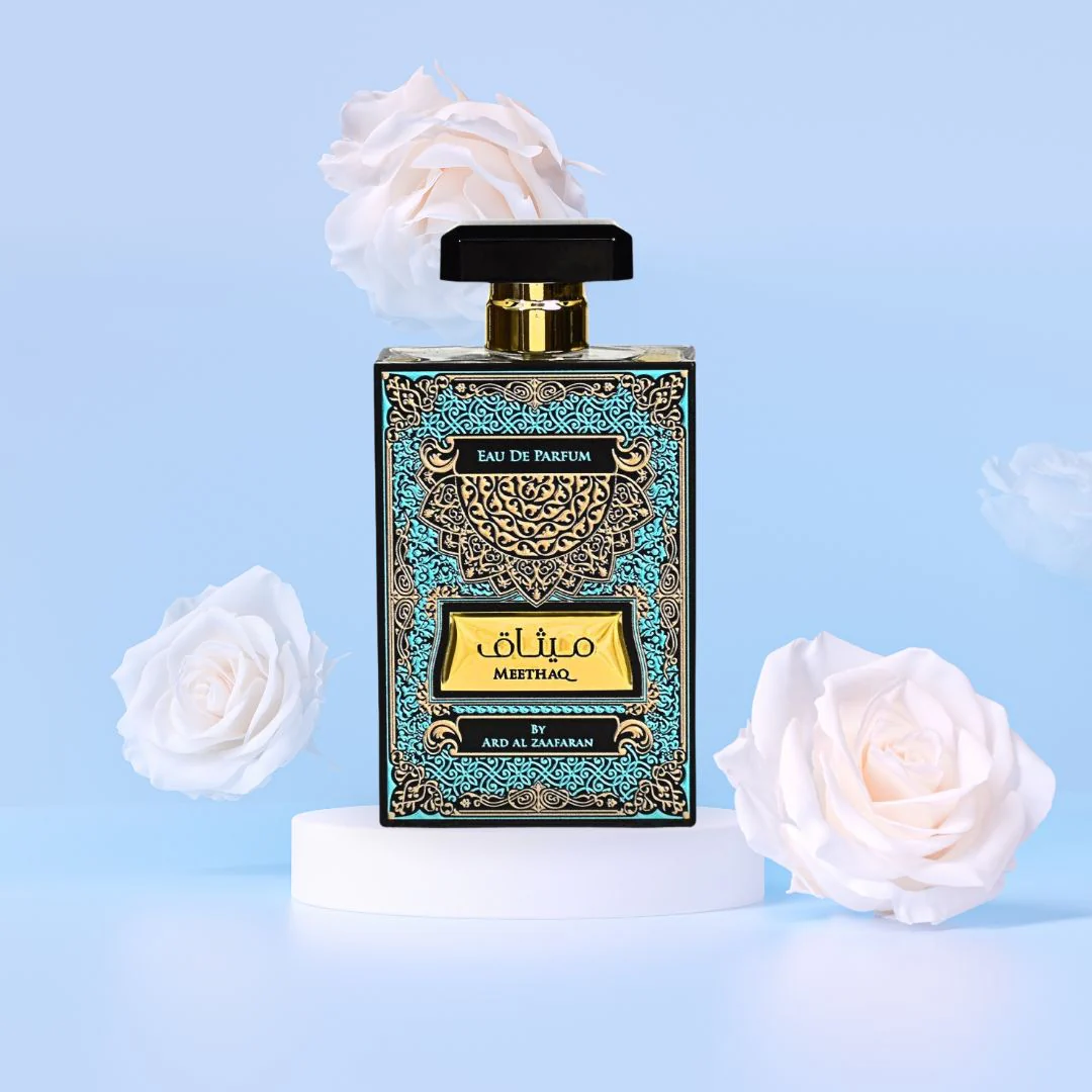 Perfume bottle with decorative packaging and white roses on a light blue background. Meethaq by Ard Al Zaafaran Unisex Perfume