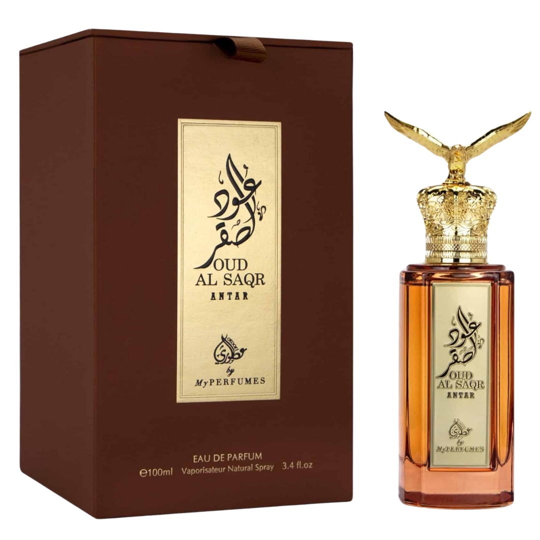 A perfume bottle of Oud Al Saqr Antar Eau de Parfum by My Perfumes, with a gold-colored cap and a brown box packaging. Premium Oud Al Saqr Antar perfume bottle with amber glass, intricate golden eagle cap, and gold-plated Arabic calligraphy label.