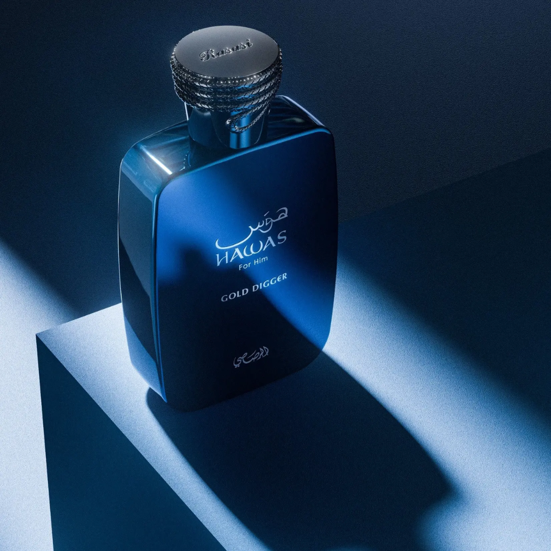A dark blue glass perfume bottle with a silver cap, labeled 'HAWAS For Men GOLD DIGGER', displayed on a geometric pedestal with dramatic blue lighting.