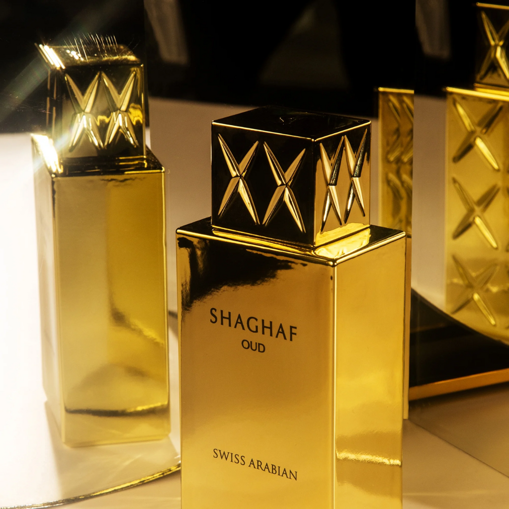 Gold perfume bottle with 'Shaghaf Oud' and 'Swiss Arabian' branding on a reflective surface.