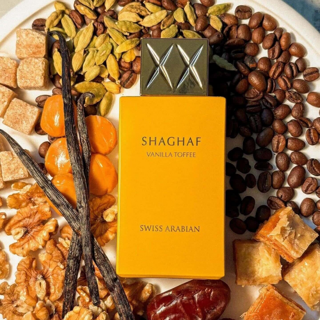 Shaghaf Vanilla Toffee perfume bottle surrounded by coffee beans, vanilla pods, and other ingredients on a white background.