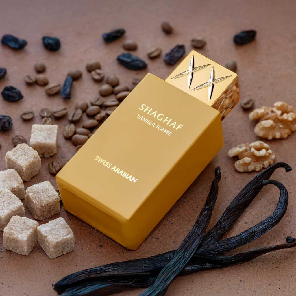Yellow perfume bottle labeled 'Shaghaf Vanilla Toffee' by Swiss Arabian on a brown background with vanilla beans and sugar cubes.