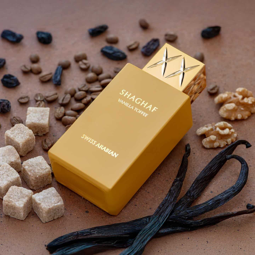 Yellow perfume bottle labeled 'Shaghaf Vanilla Toffee' by Swiss Arabian on a brown background with vanilla beans and sugar cubes.