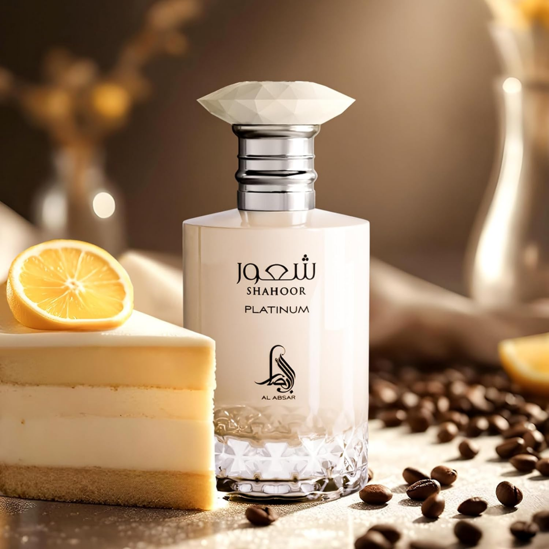 Perfume bottle labeled 'Shahoor Platinum' with a cake, lemon, and coffee beans on a wooden surface.