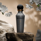Surrati Gray Oud perfume bottle on a stone pedestal beside flowers.