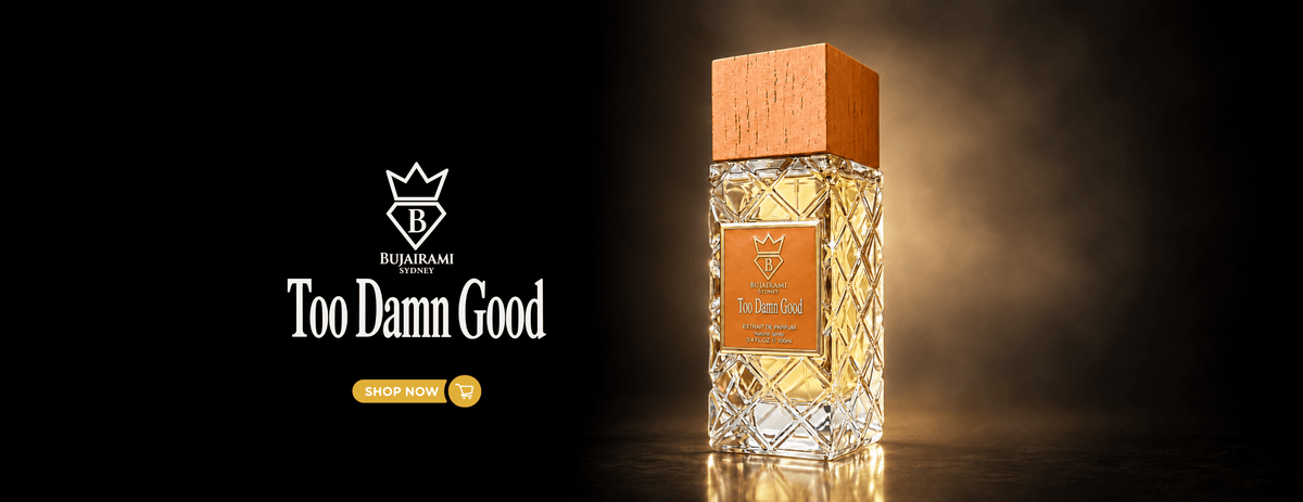 A faceted glass perfume bottle with amber liquid and a light wood cap stands on a dark reflective surface against a smoky black background. The left side features the brand logo and the text 'Too Damn Good' with a yellow 'SHOP NOW' button.